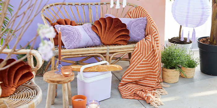 Buitenboel 1
Goeie combi: natureltinten met lila, oranje en roest. Bijvoorbeeld zo’n rotan bankje en stoel (kussens erop, plaid erbij) met een handige koelbox voor overdag en de mooiste kaarsenhouders en kandelaars voor ’s avonds. 